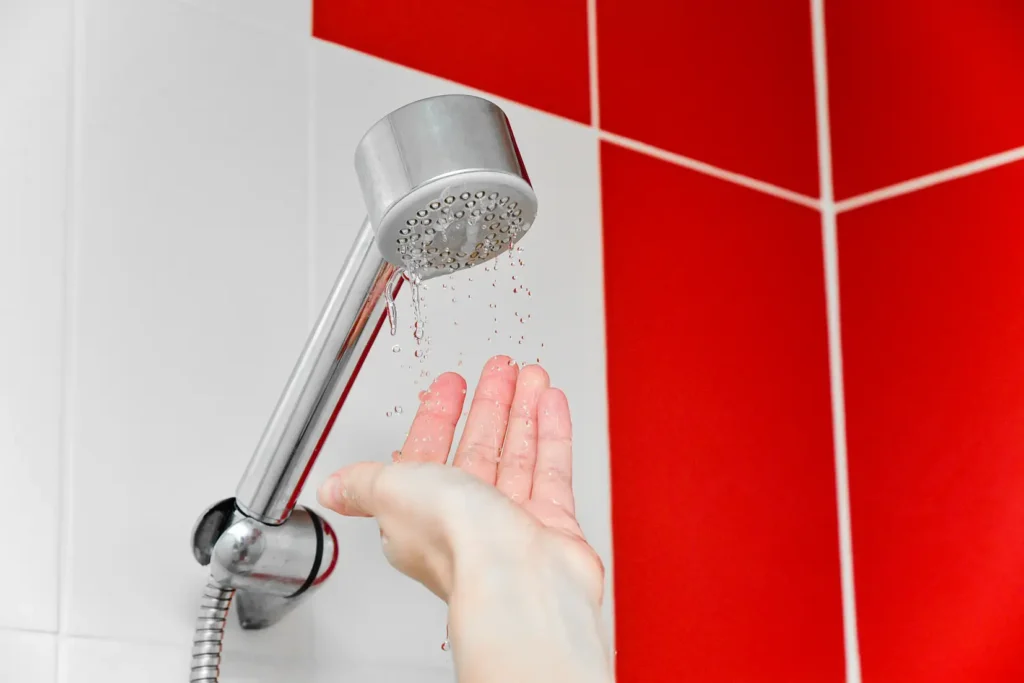 Testing shower head water pressure with hand, showing potential causes of low water flow in home plumbing