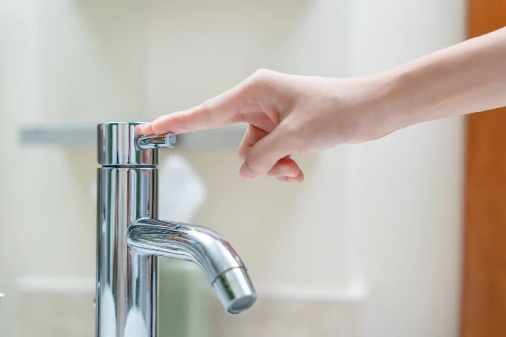 Hand turning off modern faucet, demonstrating water conservation methods to reduce household water bills