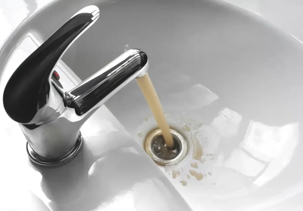 Yellow water from tap: yellowish tap water flowing from chrome faucet