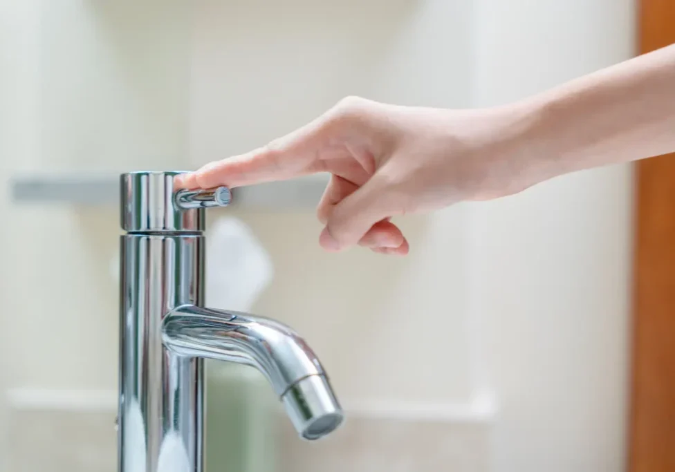 Hand turning off modern faucet, demonstrating water conservation methods to reduce household water bills